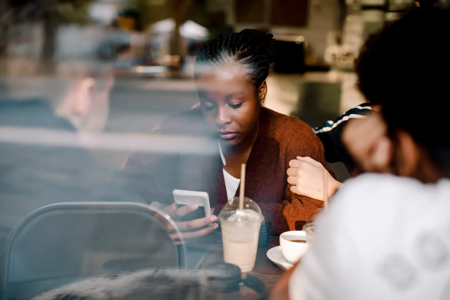 Eine junge Frau schaut mit traurigem Gesichtsaudruck auf ihr Smartphone und wird getröstet