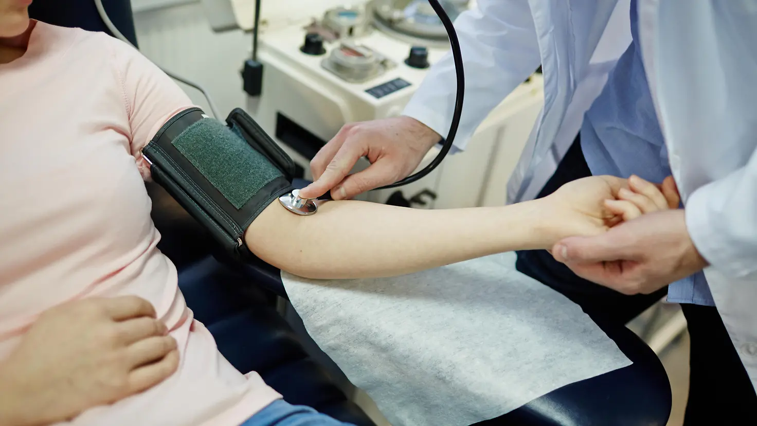 Zu sehen ist ein Arzt, der bei einer Patientin Blutdruck misst 