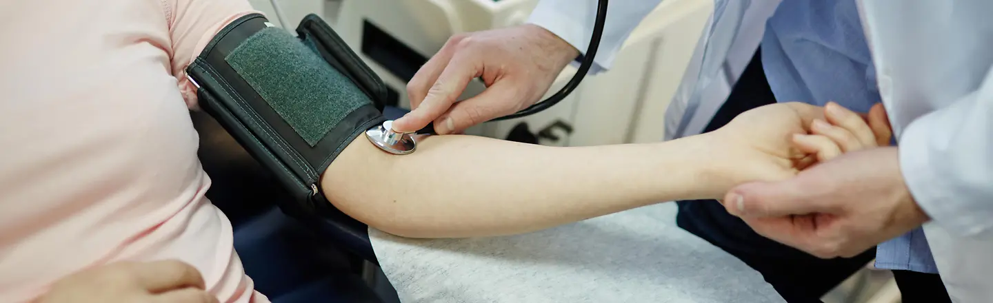 Zu sehen ist ein Arzt, der bei einer Patientin Blutdruck misst 
