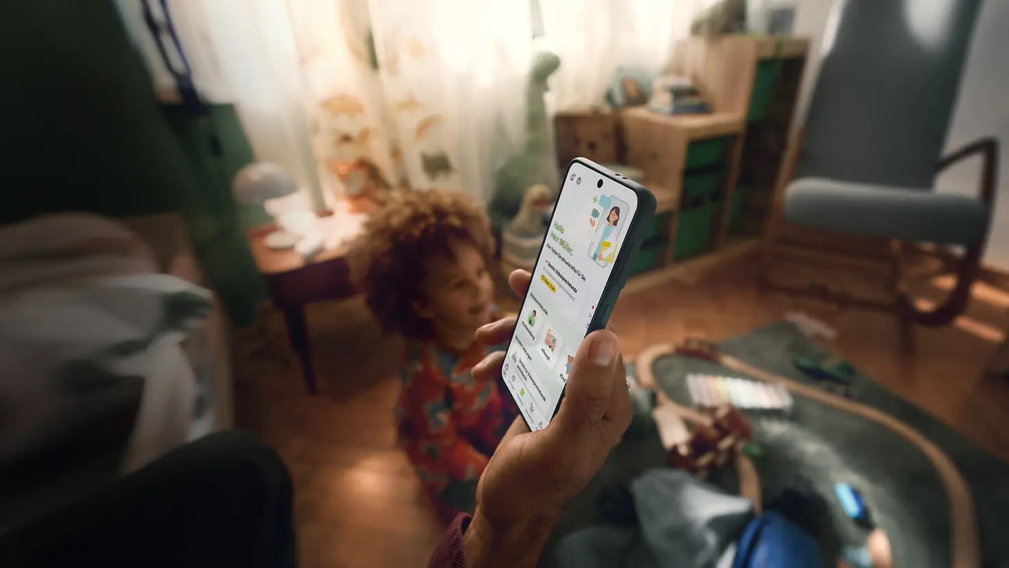 Ein Familienvater hält sein Handy in der Hand, auf dem der Startbildschirm der Teledoktor-App zu sehen ist. 