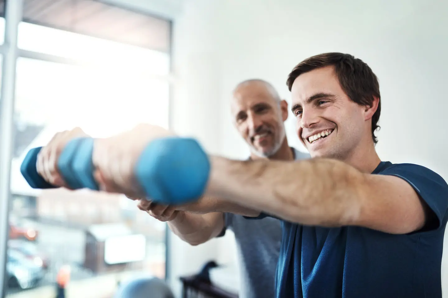 Ein Mann wird mit Hanteln von einem Personal Trainer trainiert