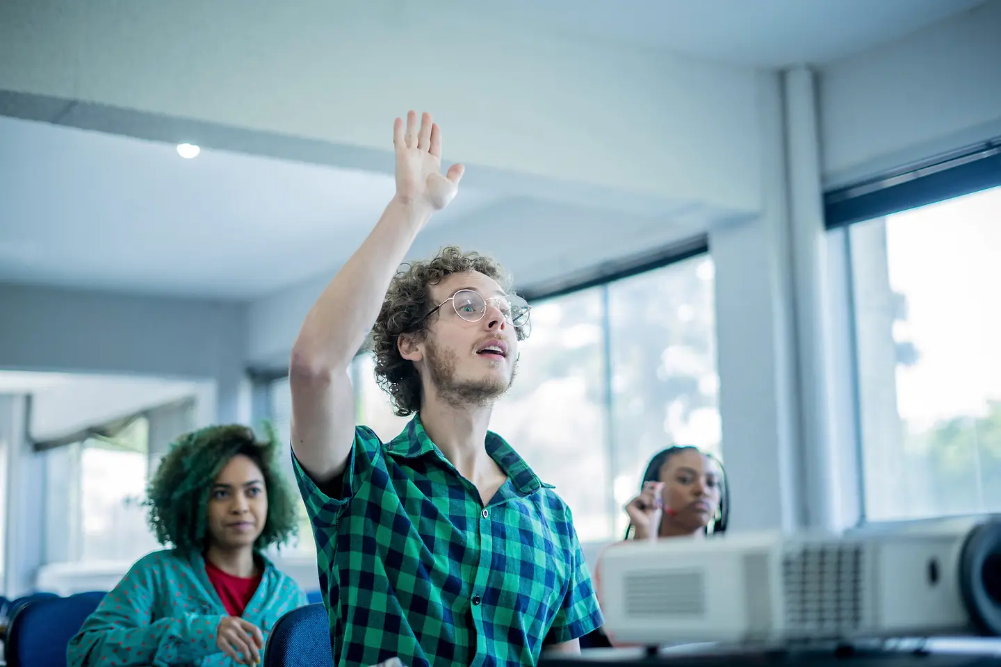 Ein junger Mann in einem Klassenzimmer meldet sich mit Handzeichen