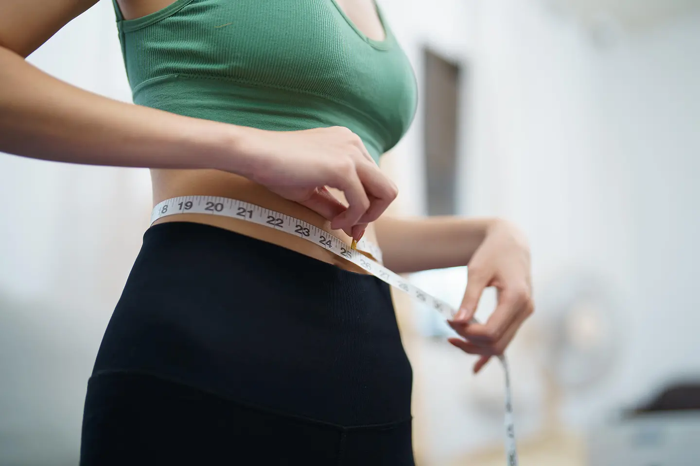 Zu sehen ist eine dünne Frau, die sich mit einem Maßband die Taille misst 