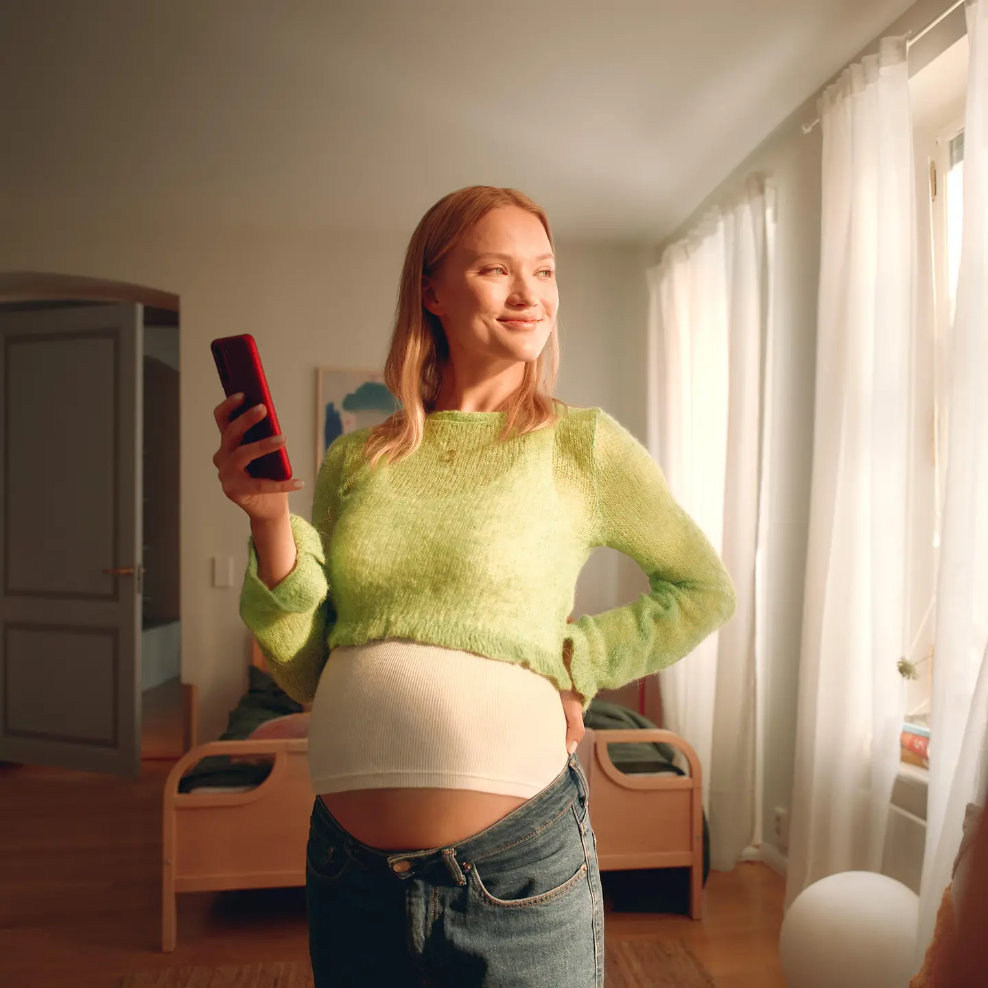 Eine schwangere Frau hält ein Handy in der Hand. 