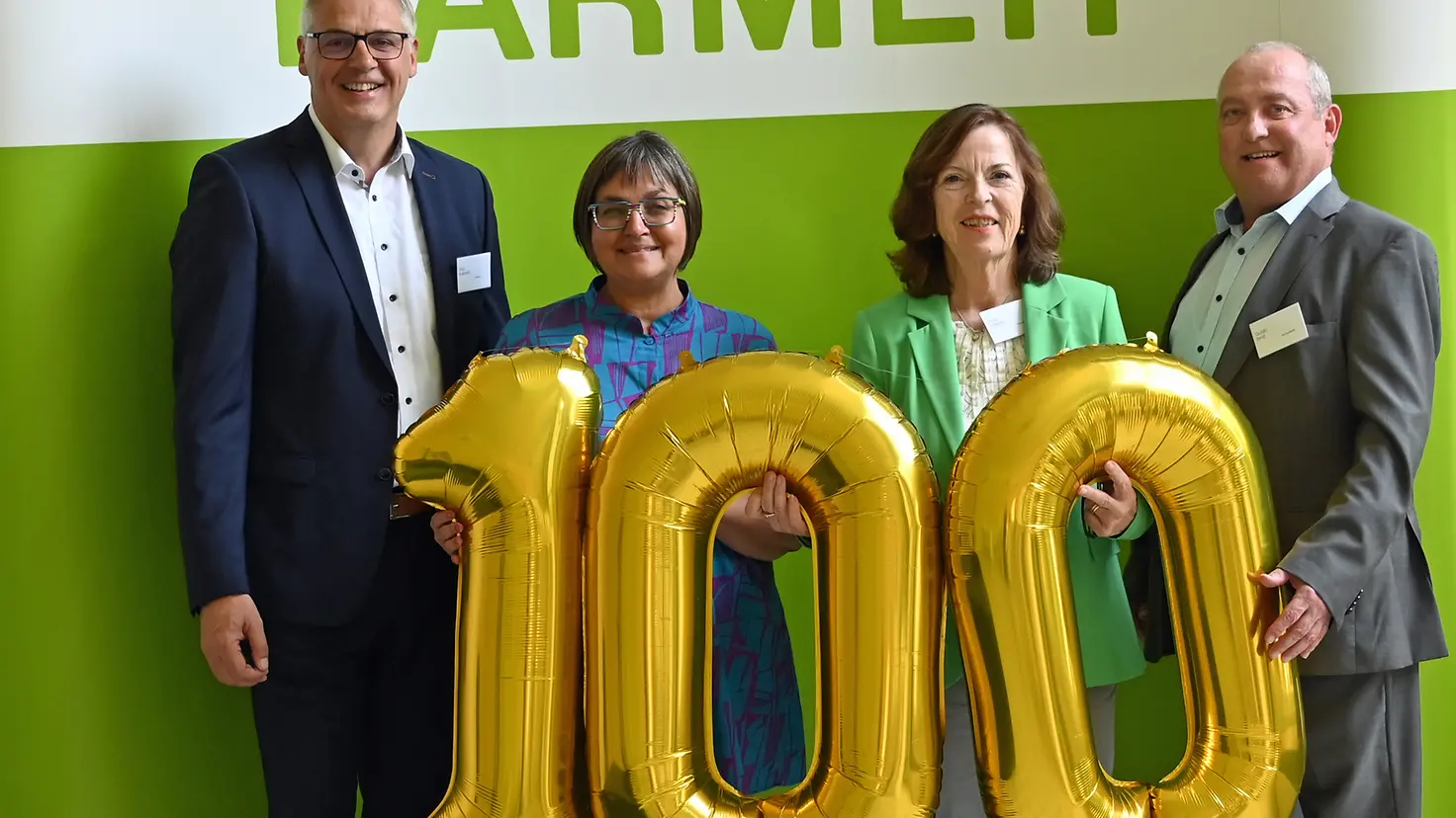 BARMER-Beschäftigte und die Trierer Bürgermeisterin stehen vor ein Wand und halten einen goldenen 100-Luftballon vor sich.
