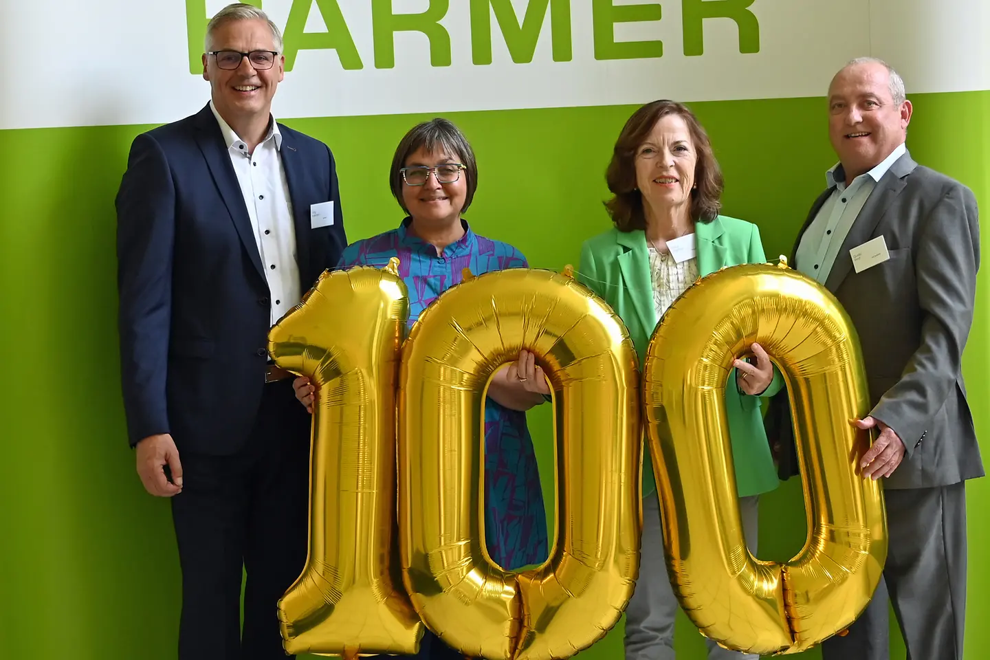 BARMER-Beschäftigte und die Trierer Bürgermeisterin stehen vor ein Wand und halten einen goldenen 100-Luftballon vor sich.