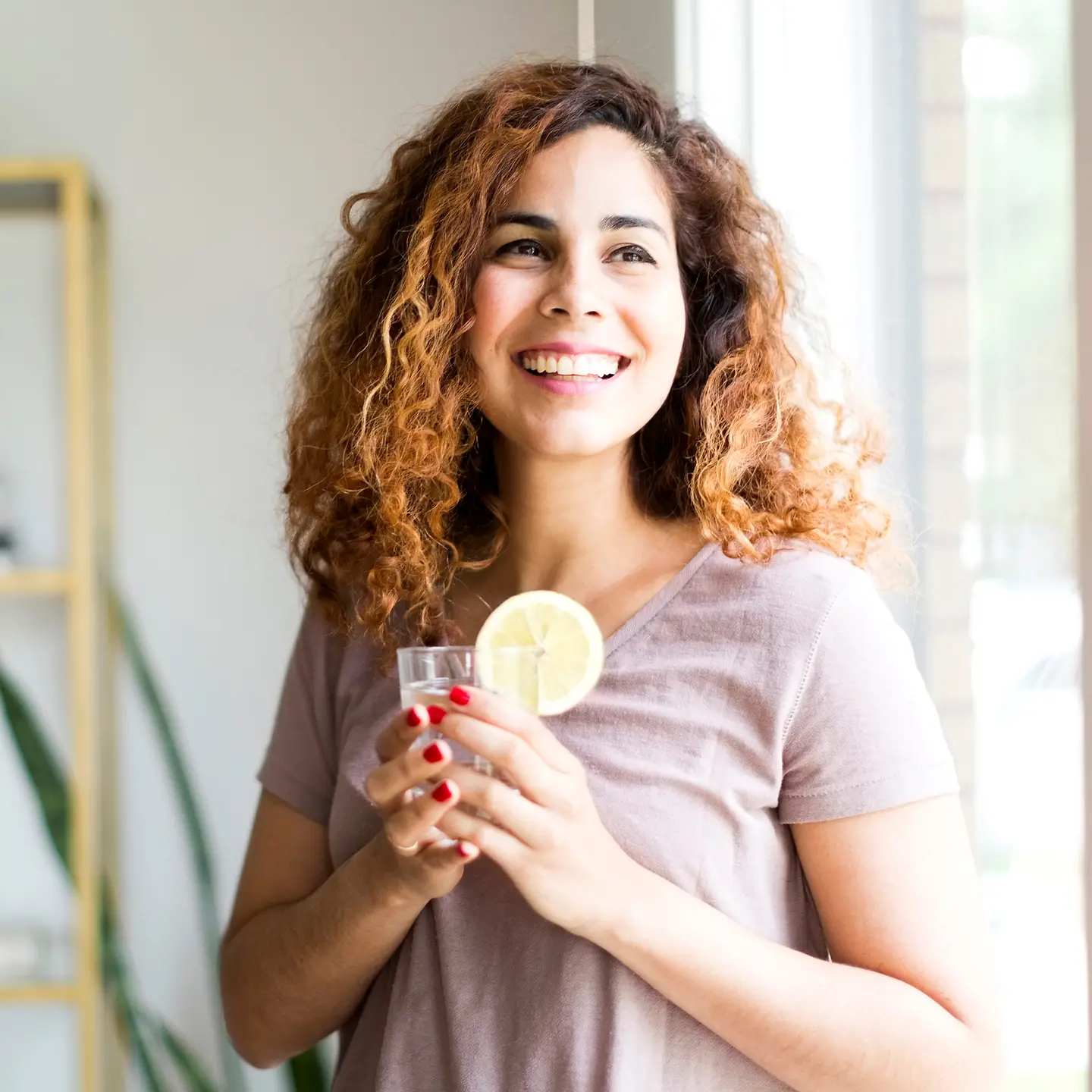 Eine Frau lacht und hält ein Glas Wasser mit einer Zitronenscheibe in der Hand.Testbild