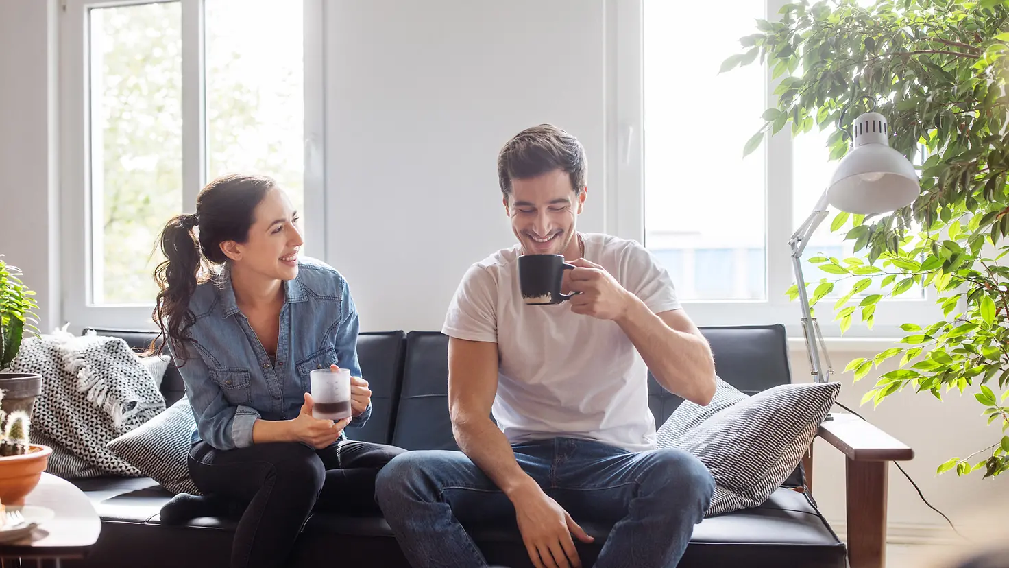Ein junges Paar sitzt gemeinsam auf der Couch und trinkt Kaffee.