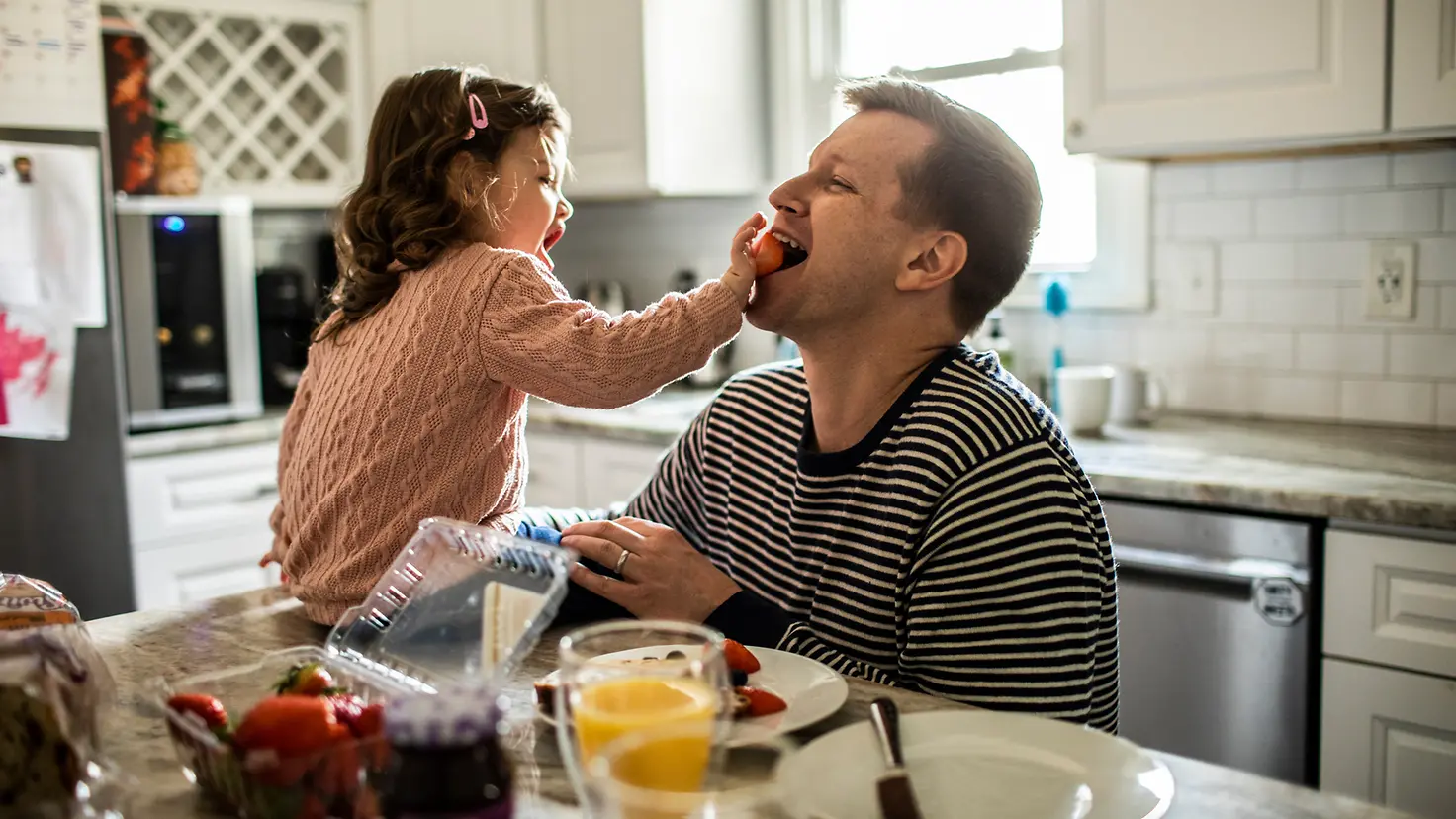 Ein junger Papa mit Tochter essen am Küchentisch Erdbeeren