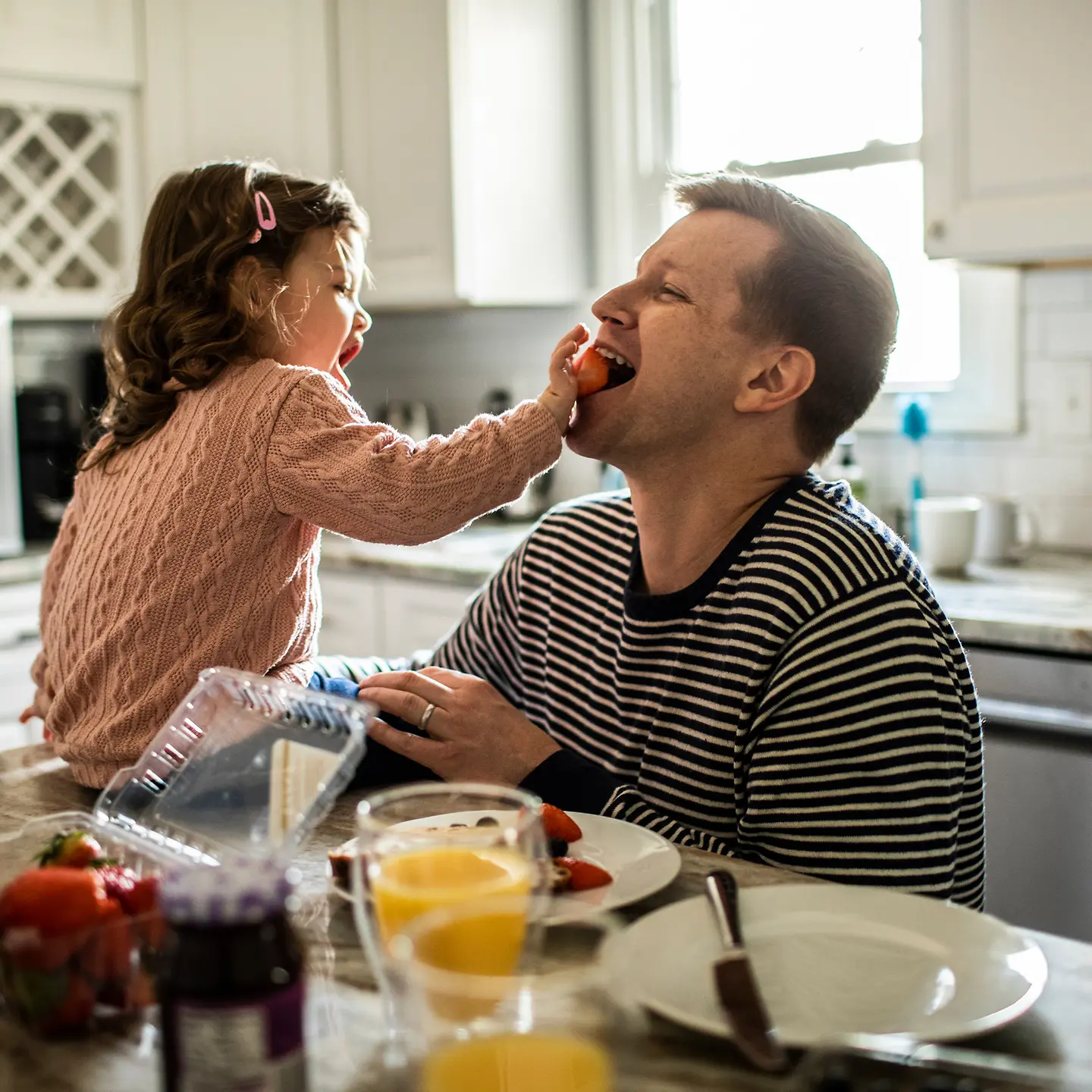 Ein junger Papa mit Tochter essen am Küchentisch Erdbeeren