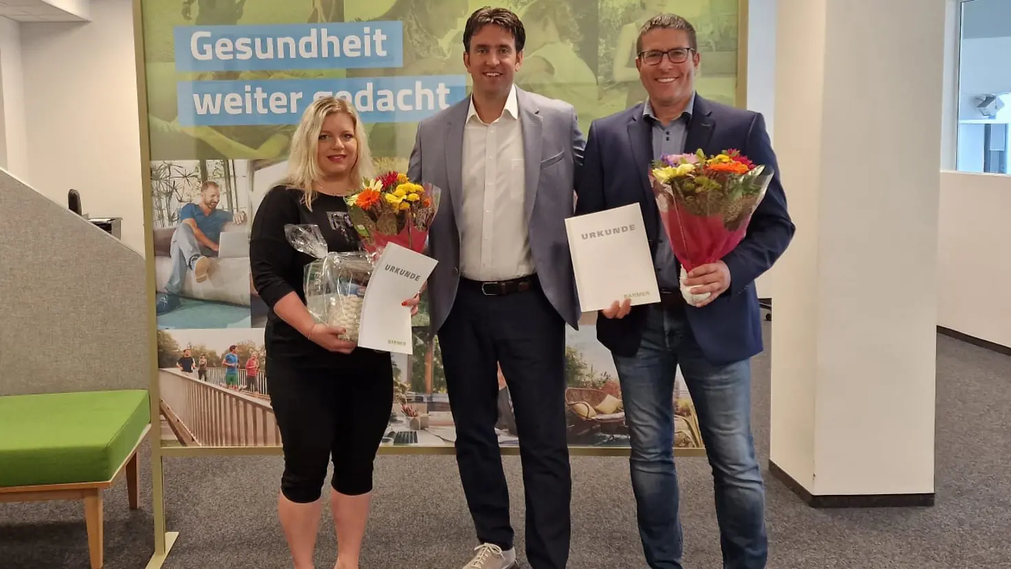 Die Jubilare stehen mit Blumen und Urkunde in der Hand neben dem Regionalgeschäftsführer vor einer Wand.