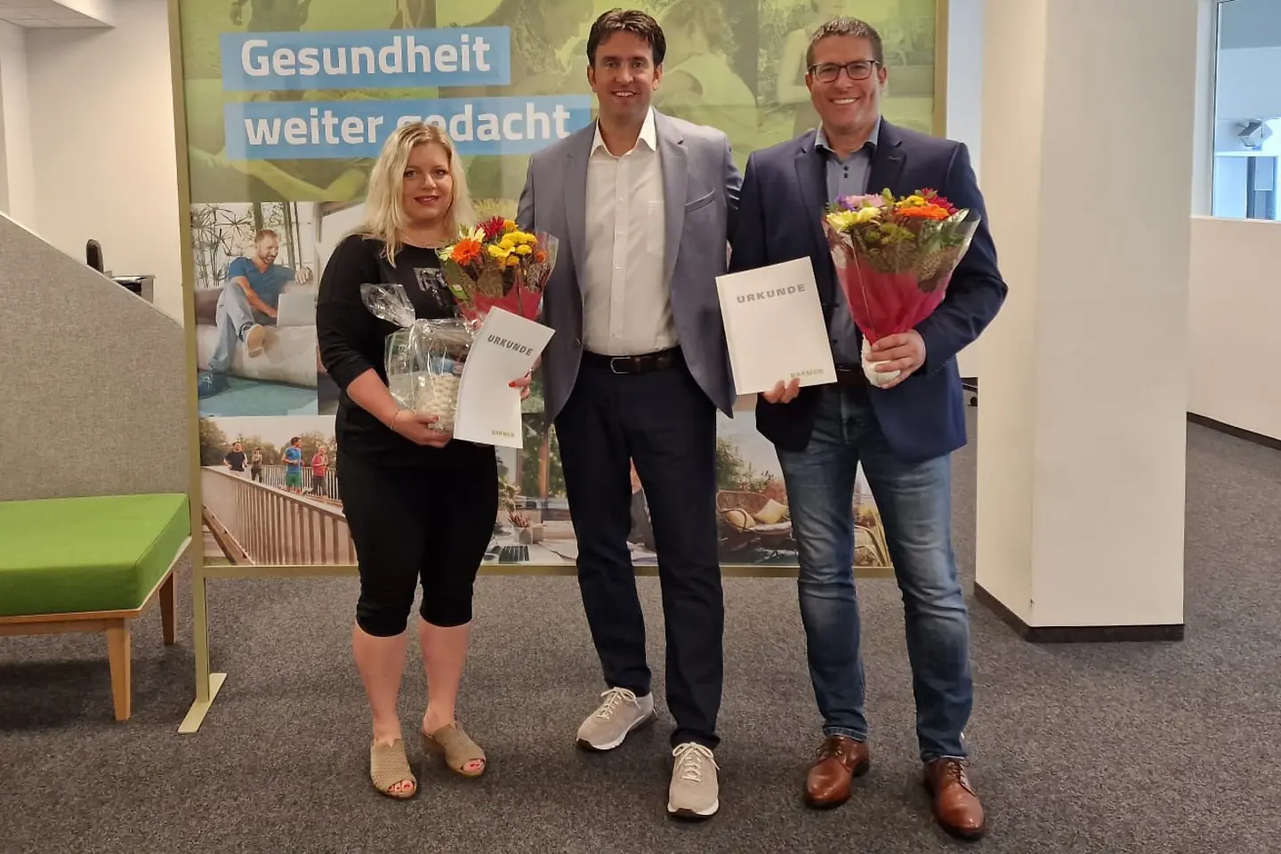 Die Jubilare stehen mit Blumen und Urkunde in der Hand neben dem Regionalgeschäftsführer vor einer Wand.