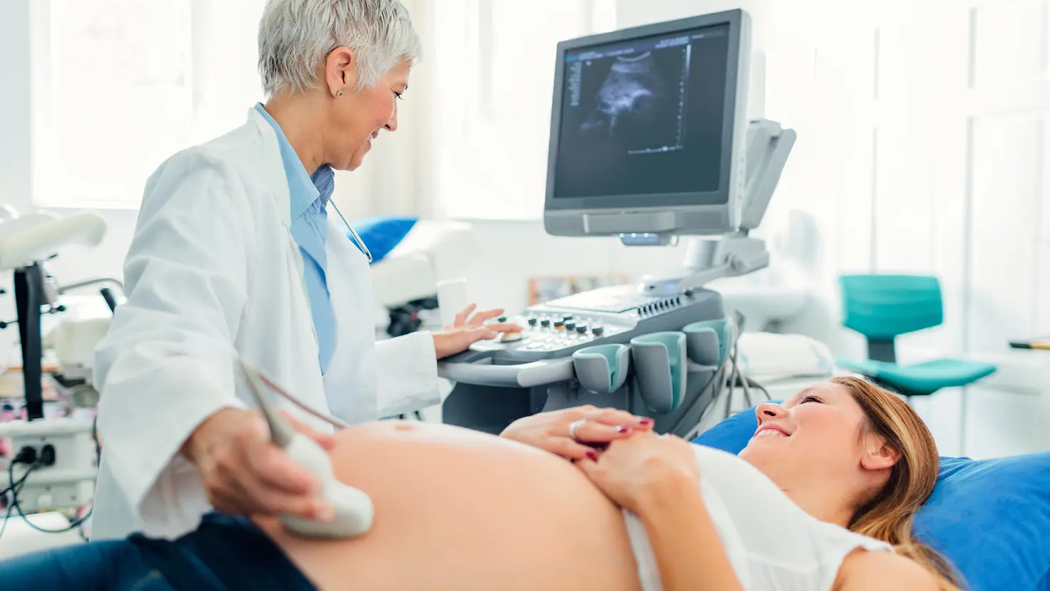 Eine schwangere Frau auf einer Behandlungsliege erhält eine Ultraschalluntersuchung von einer Ärztin.