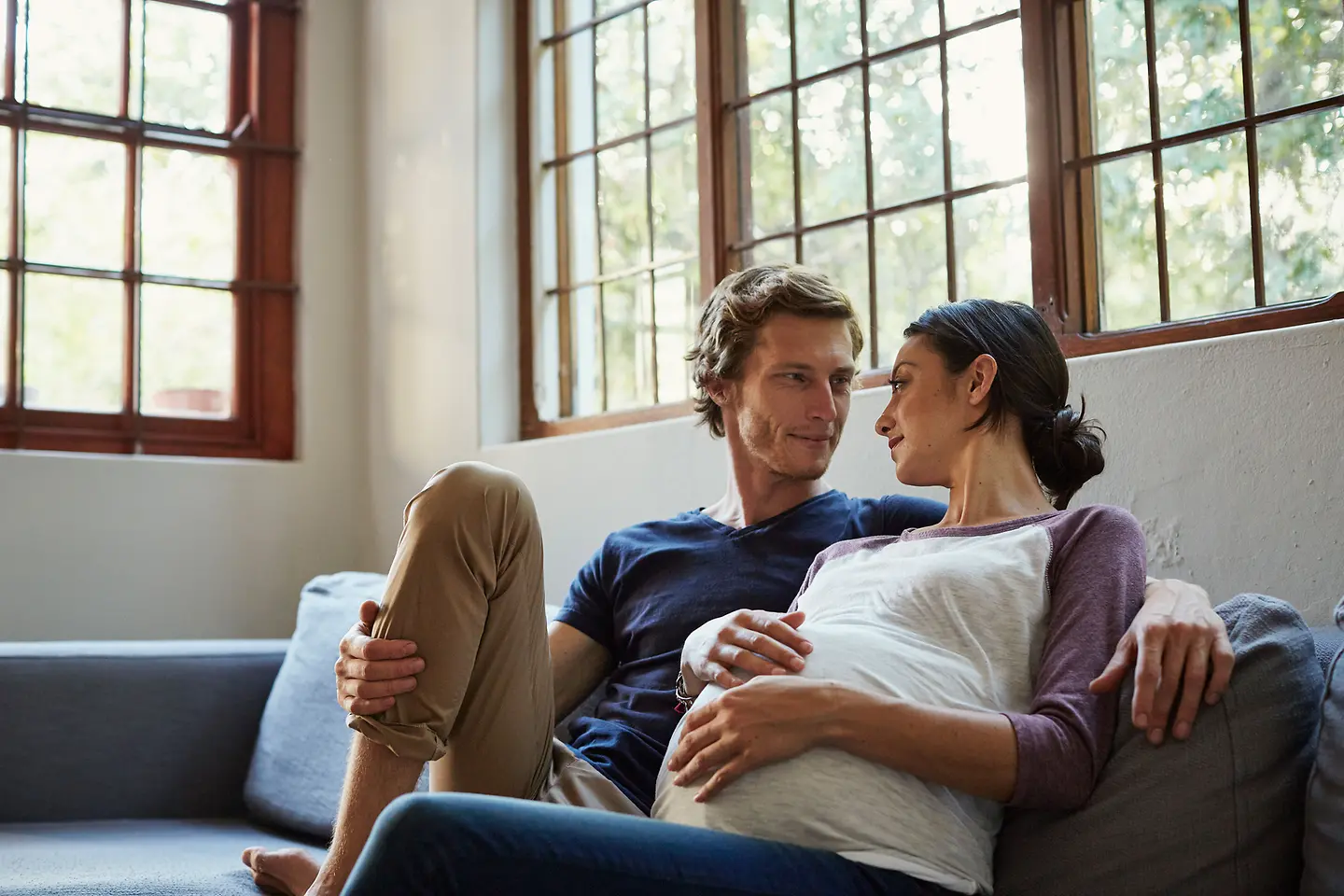 Eine hochschwangere Frau und ihr Partner schauen sich an, während sie sich auf dem Sofa entspannen