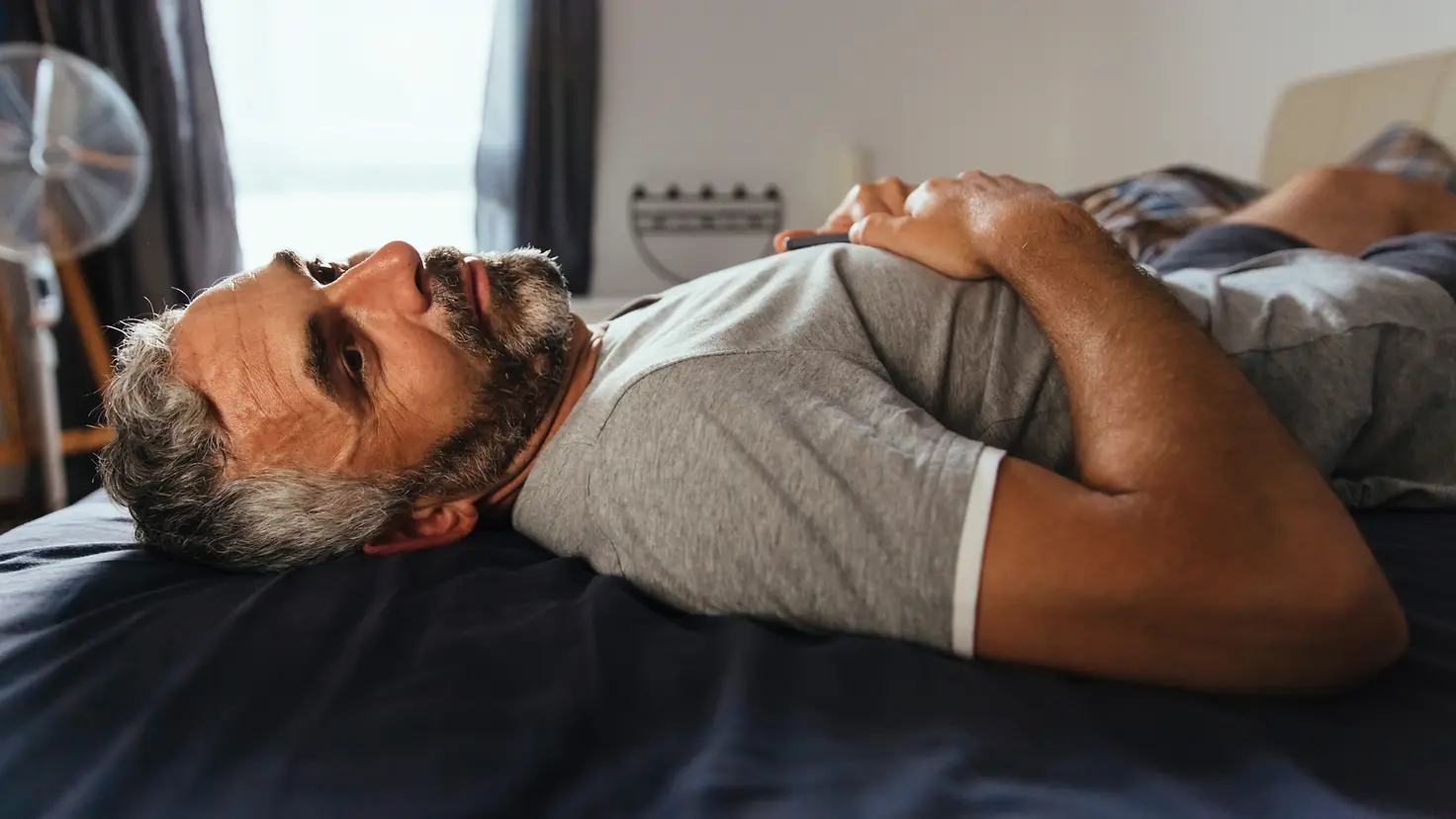 Mann liegt erschöpft mit Grippesymptomen auf dem Bett