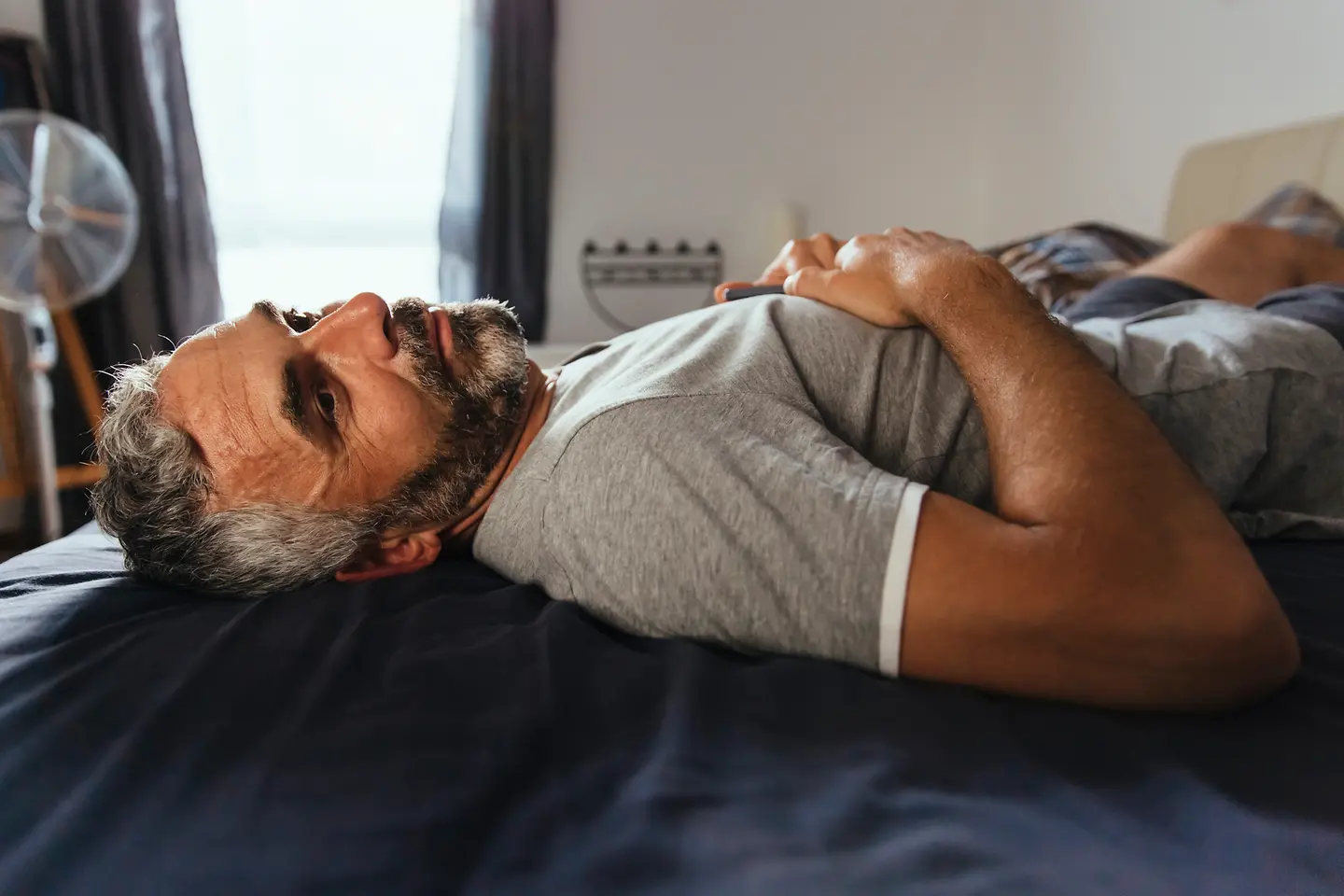 Mann liegt erschöpft mit Grippesymptomen auf dem Bett