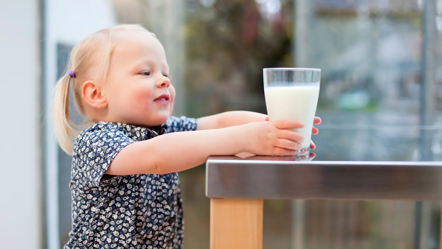 Ein kleines Mädchen greift nach einem Glas Milch