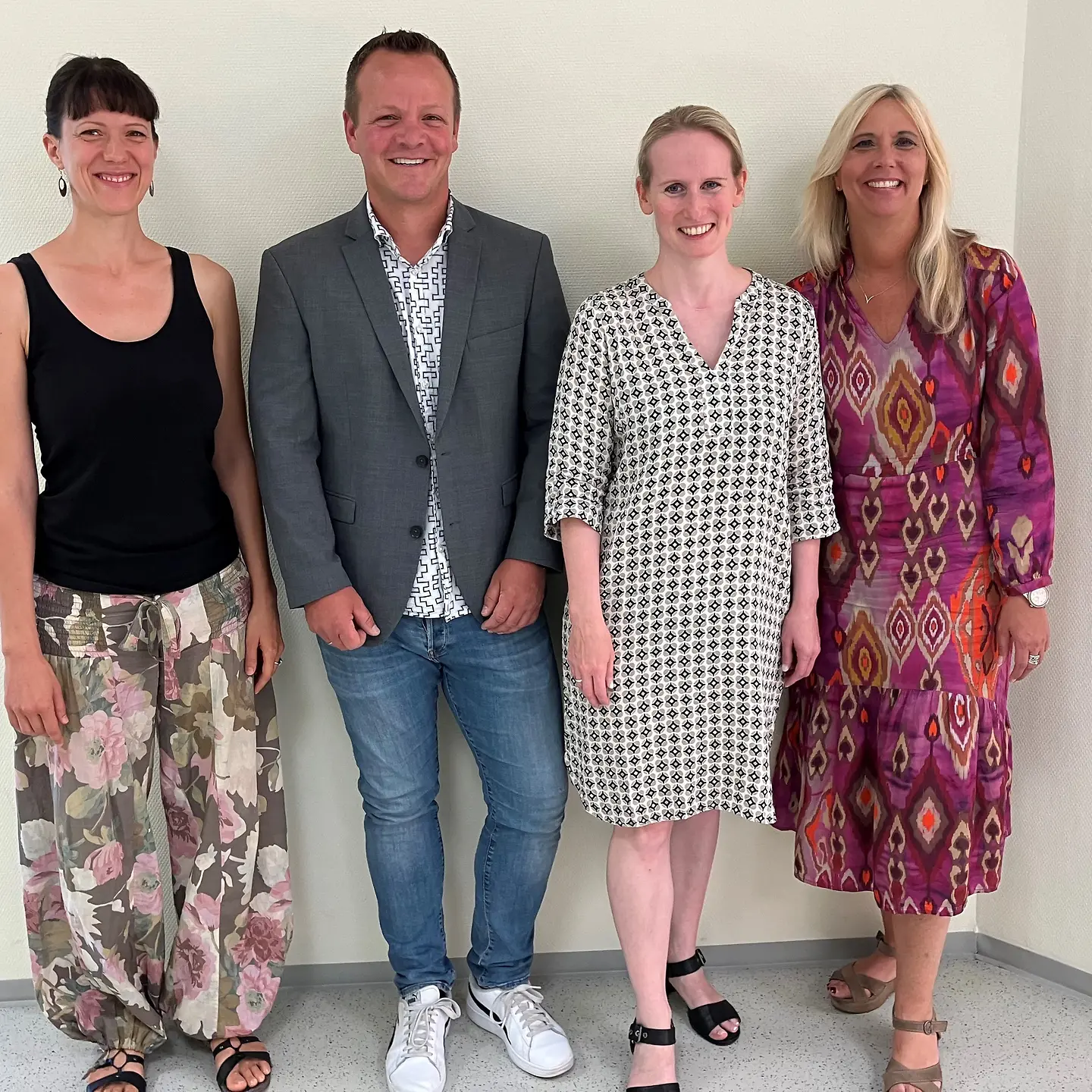 Drei Frauen und ein Mann stehen nebeneinander und lächeln in die Kamera.