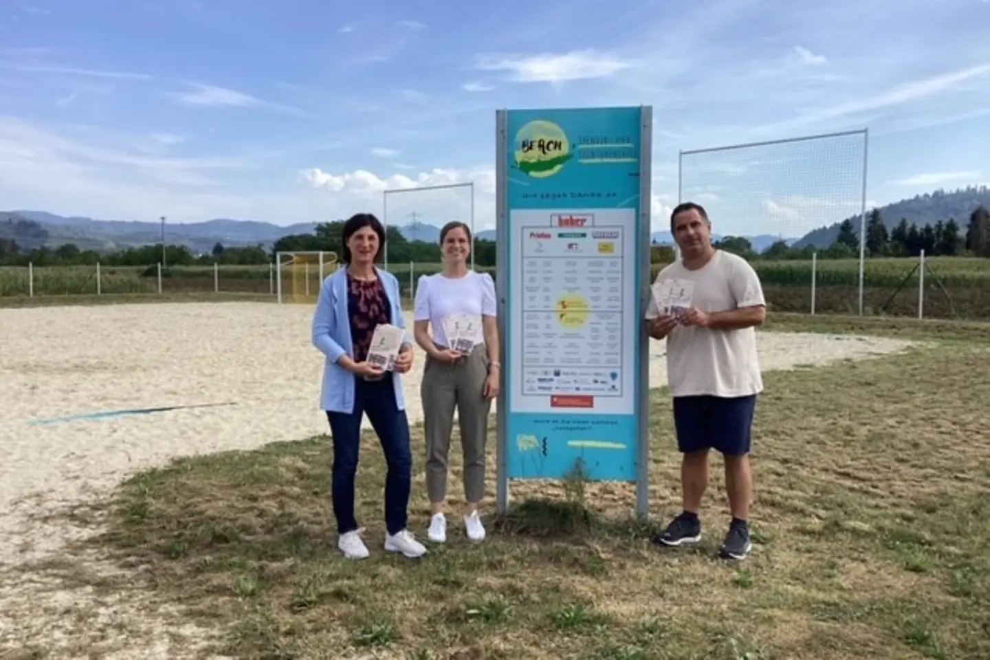 Zwei Frauen und ein Mann stehen auf einem Sportplatz und halten die Sport-Spaß Broschüre in den Händen.