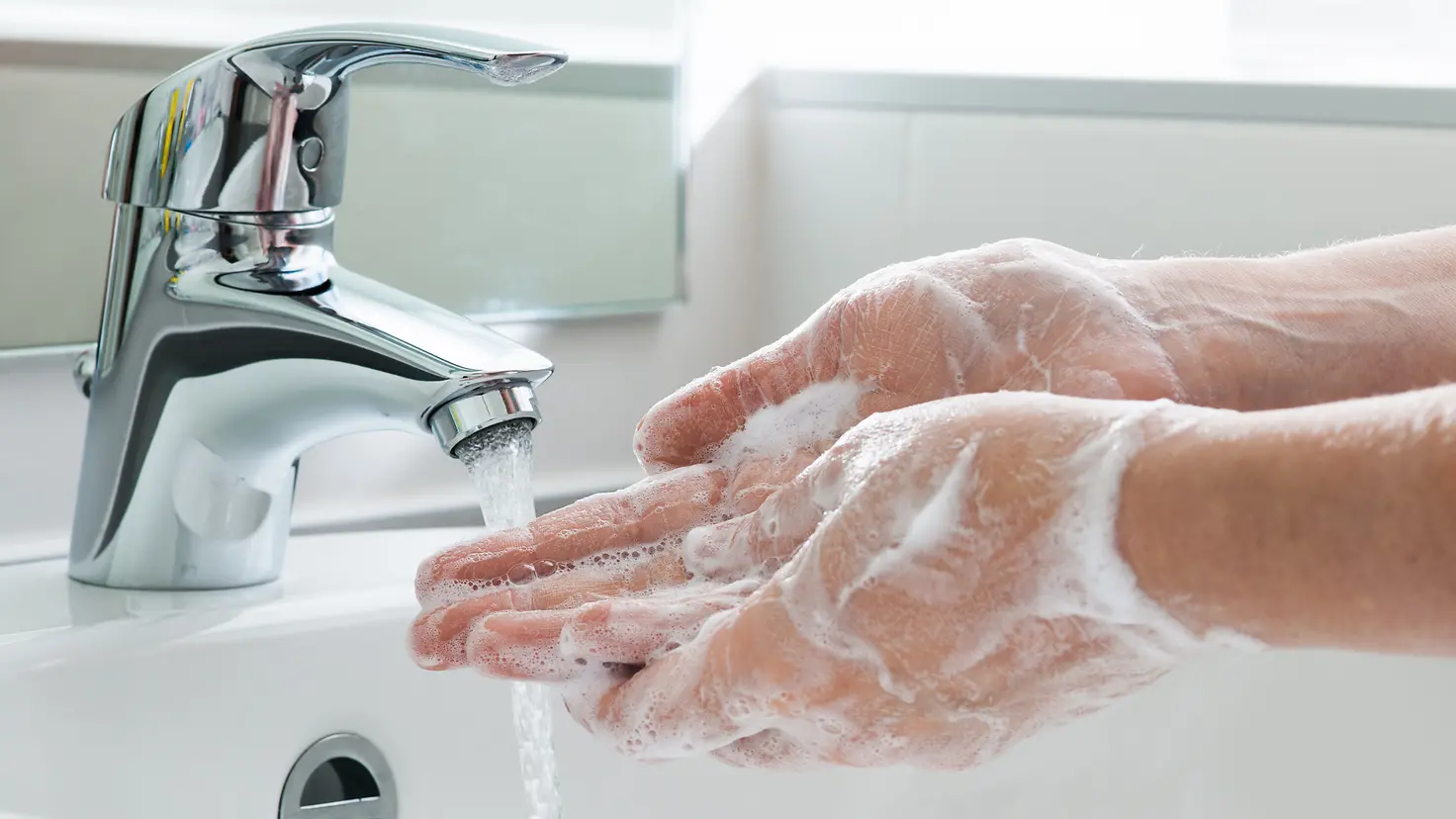 Zu sehen ist, wie Hände mit viel Seife unter fließendem Wasser gewaschen werden