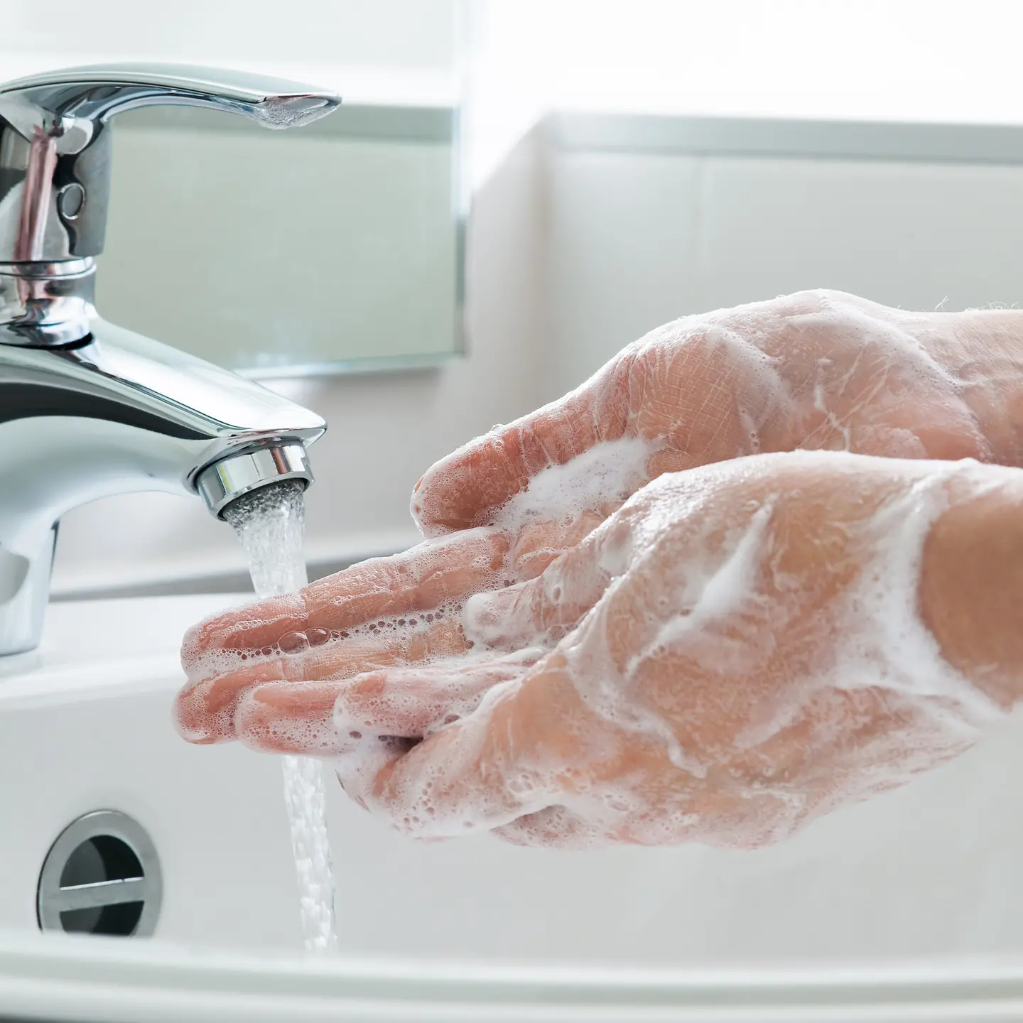 Zu sehen ist, wie Hände mit viel Seife unter fließendem Wasser gewaschen werden