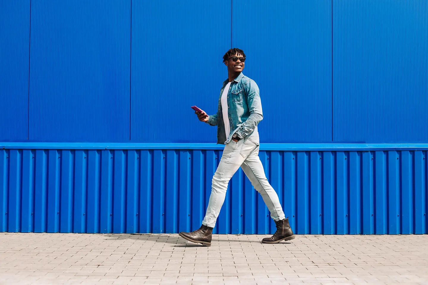 Zu sehen ist Mann mit Handy in der Hand, der lächelnd und mit großen Schritten spazieren geht