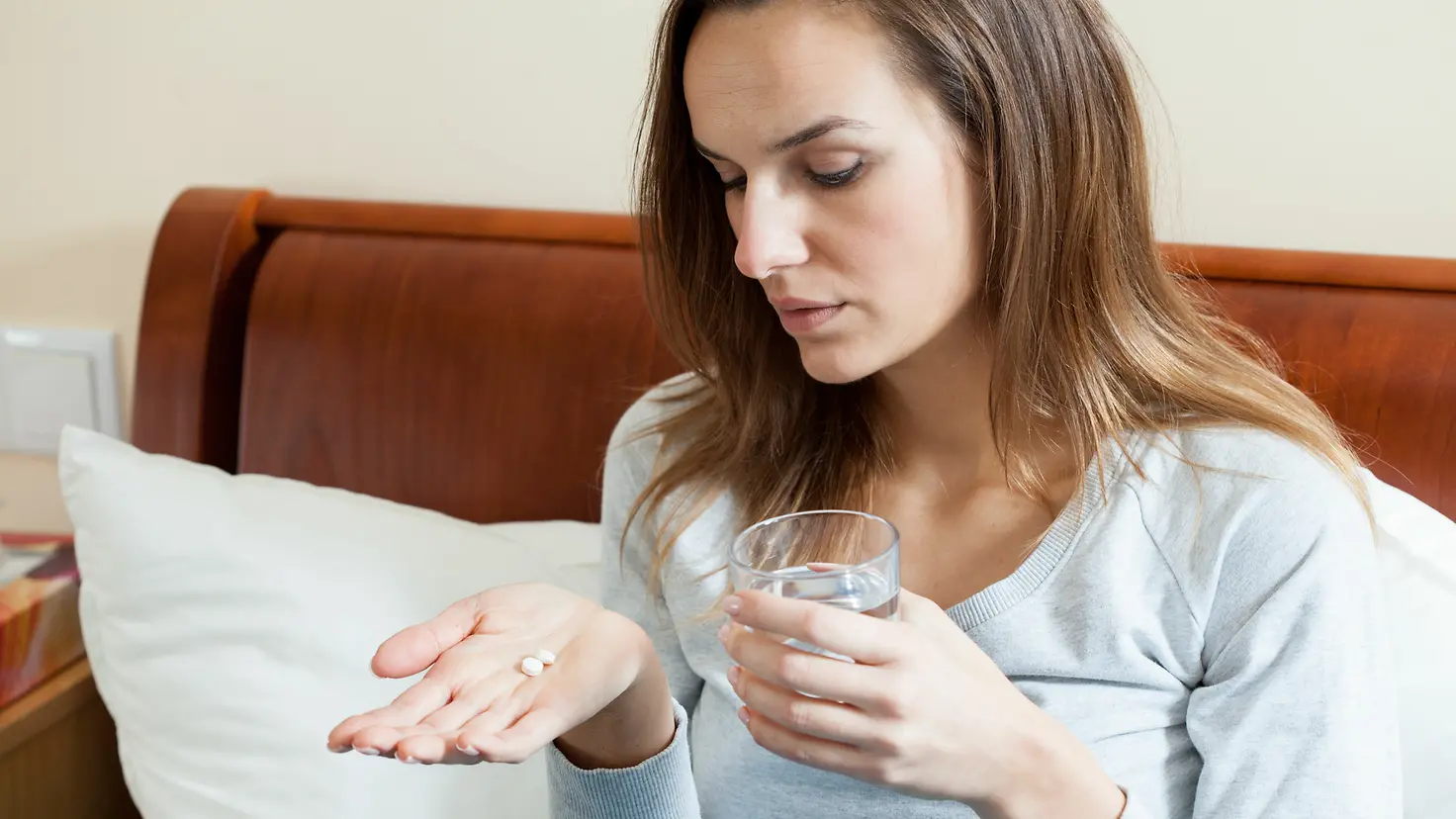 Zu sehen ist eine Frau, die mit einem Glas Wasser Tabletten einnimmt