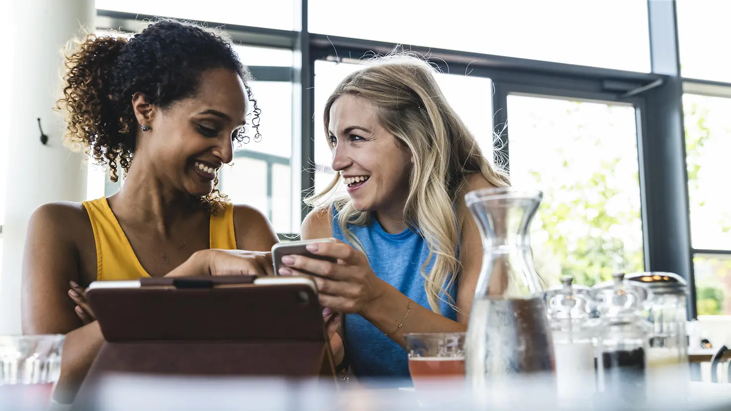 zwei junge Frauen im Sportkleidung mit mobilen Devices unterhalten sich.