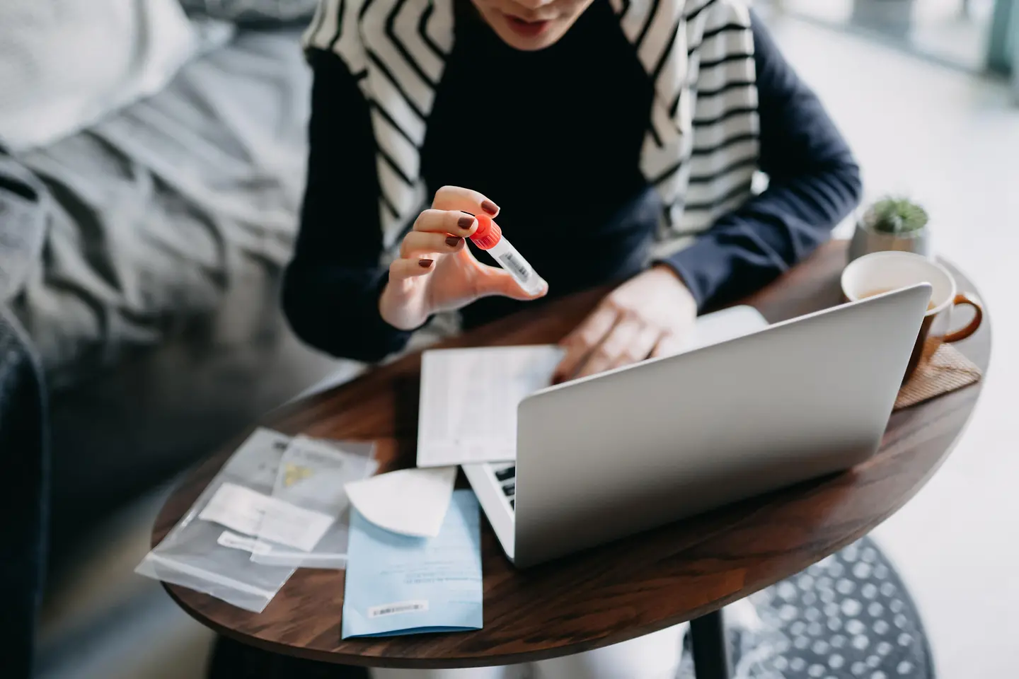 Frau hält Ampulle in die Laptopkamera und hat Beipackzettel vor sich liegen