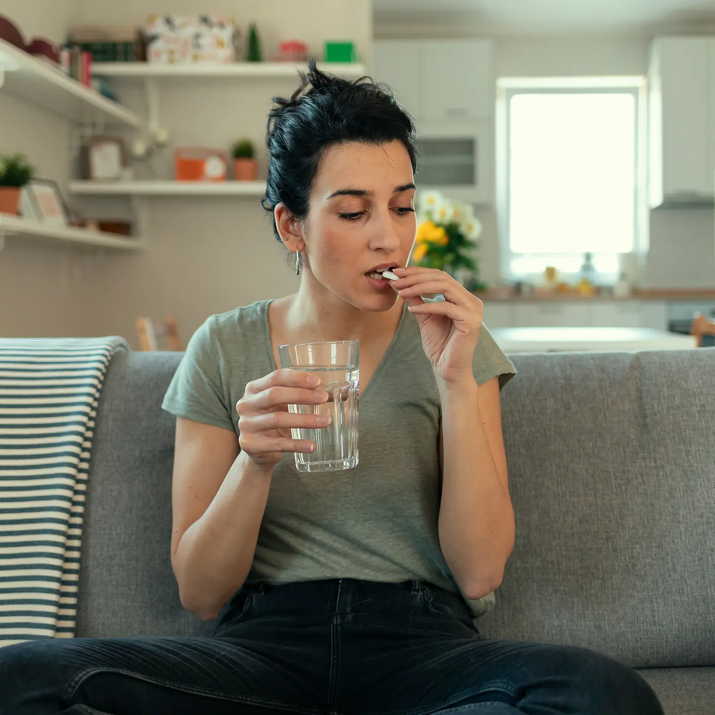 Eine Frau auf dem Sofa mit Tabletten und Wasserglas