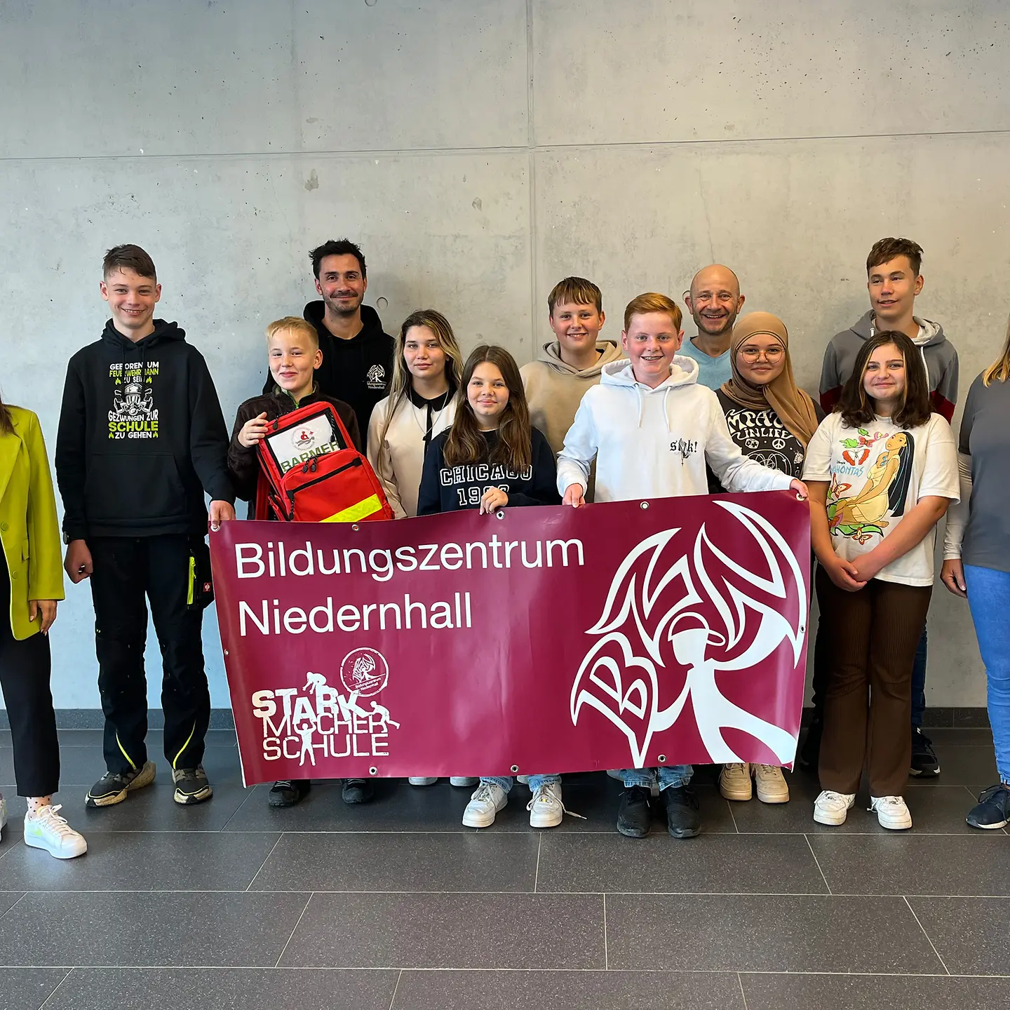 Schülerinnen und Schüler halten einen Schulsanitätsrucksack und ein Transparent mit der Aufschrift "Bildungszentrum Niedernhall" in die Kamera