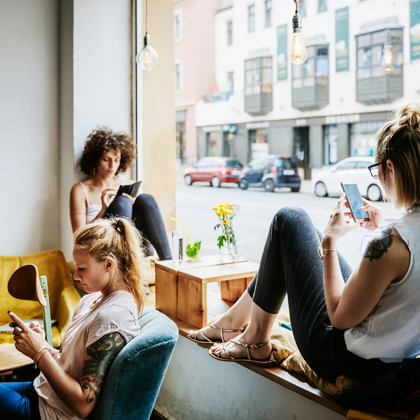Drei junge Frauen sitzen mit ihren Smartphones in einem Café