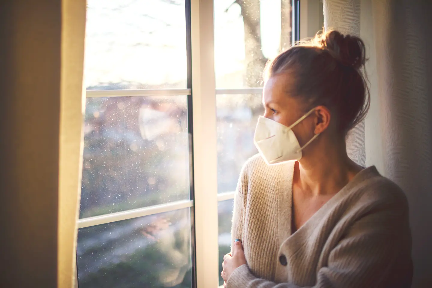 Eine Frau mit FFP2-Maske steht am Fenster.