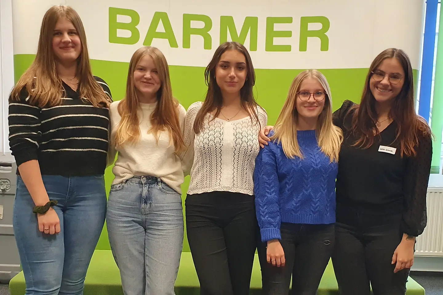 Fünf Auszubildende stehen Arm in Arm vor einer Wand.