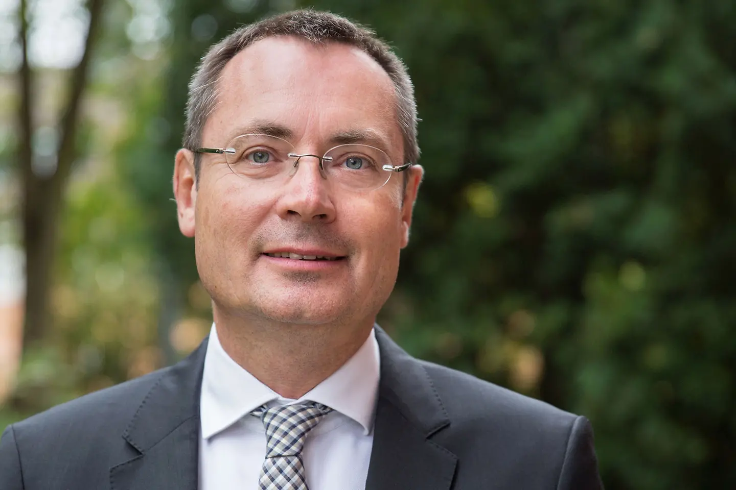 Ein Mann mit Brille, Anzug und Krawatte lächelt in die Kamera