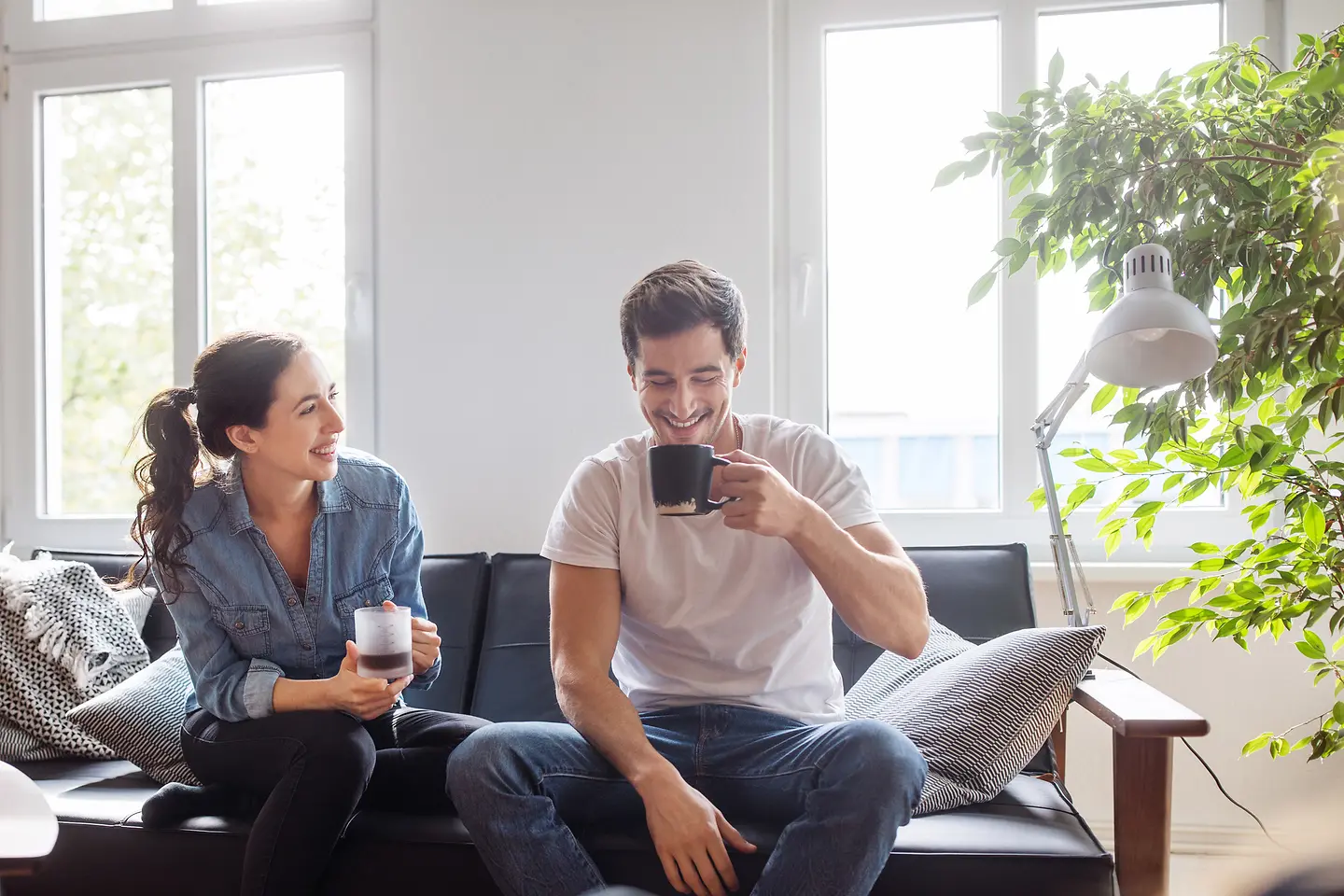 Ein junges Paar sitzt gemeinsam auf der Couch und trinkt Kaffee.