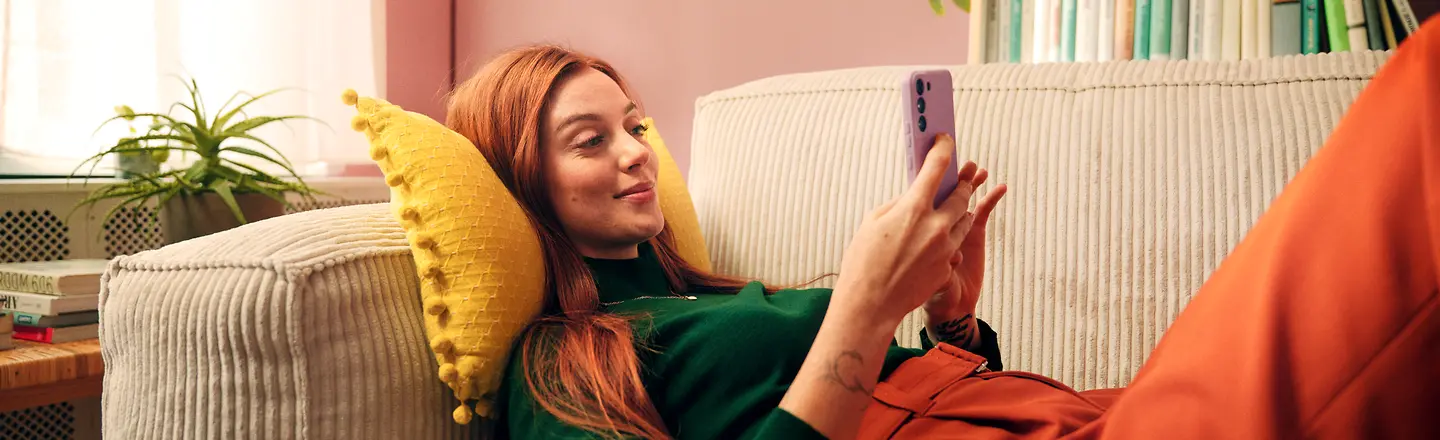 Eine Frau sitzt auf einem Sofa und hält ein Smartphone in der Hand, auf dem sie die Barmer-App nutzt.