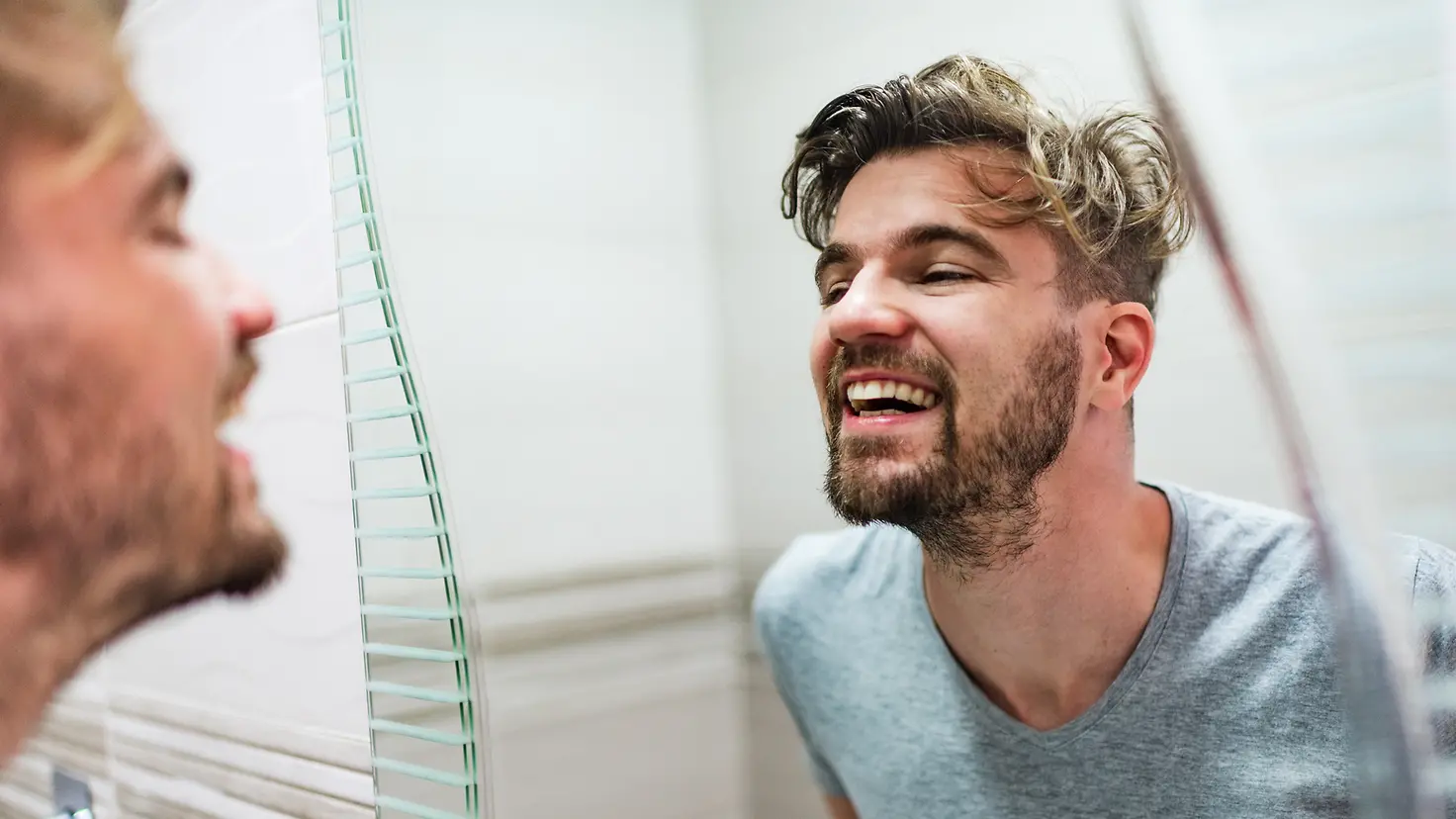 Ein Mann prüft seine Zähne im Spiegel auf Karies.