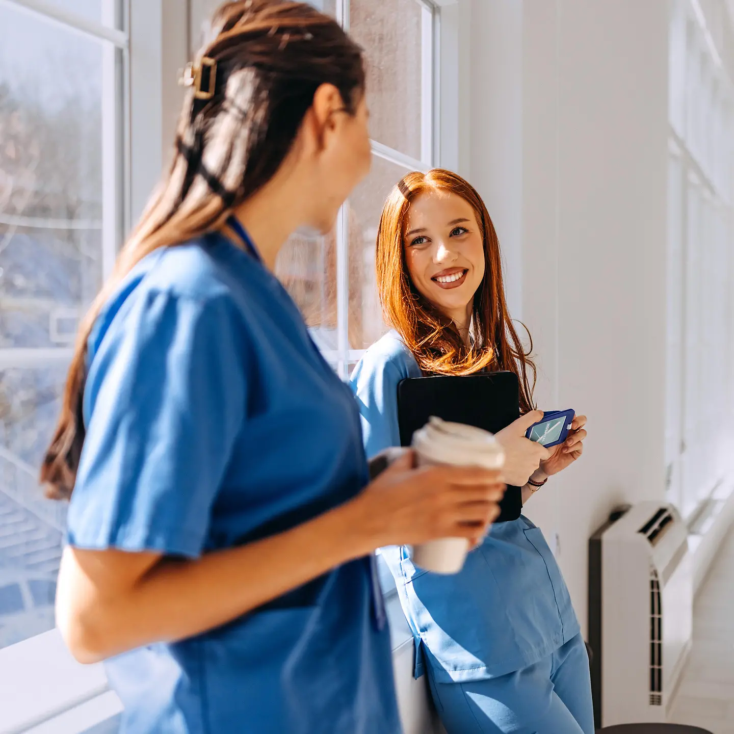 Zwei junge Pflegerinnen stehen locker zusammen und unterhalten sich