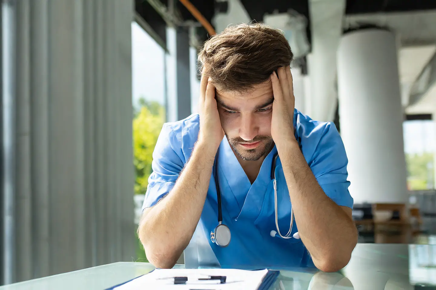 Zu sehen ist ein Krankenpfleger, der seinen Kopf abstützt und deprimiert aussieht