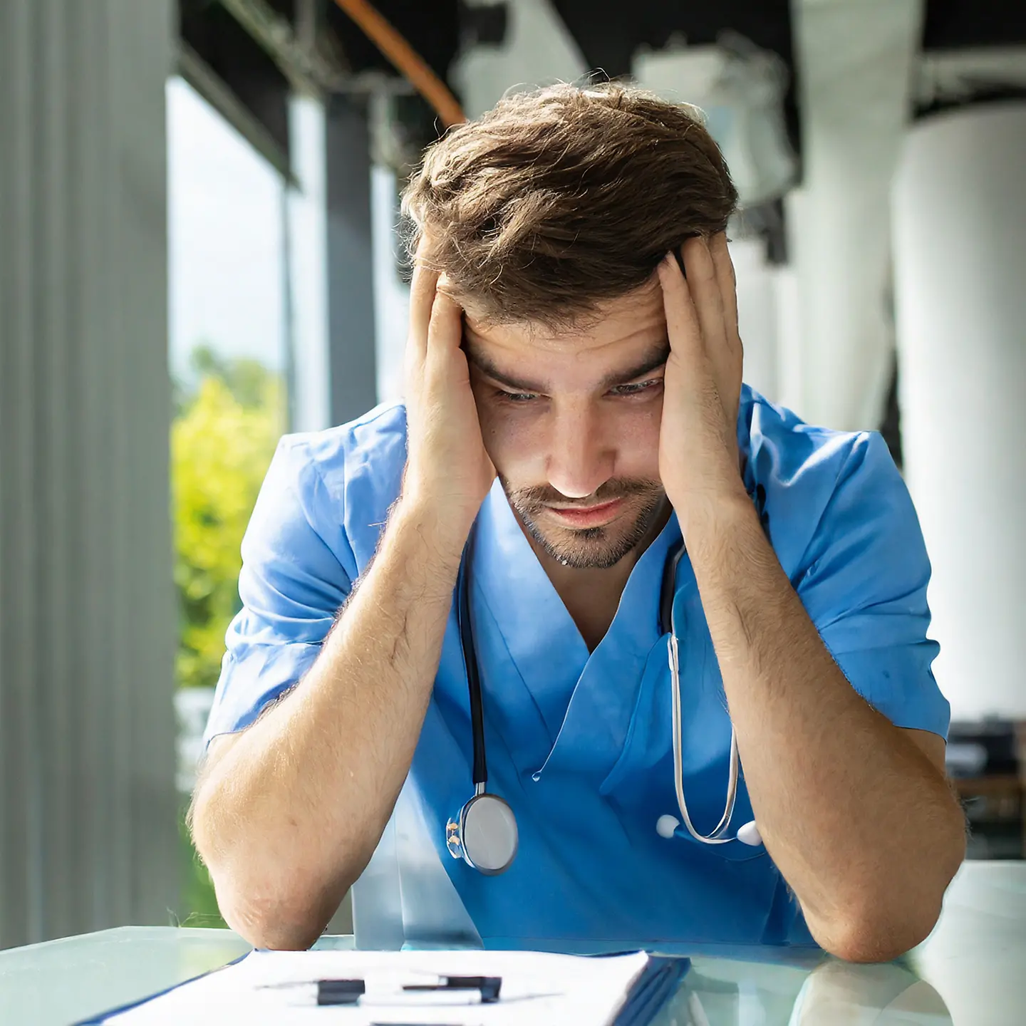 Zu sehen ist ein Krankenpfleger, der seinen Kopf abstützt und deprimiert aussieht