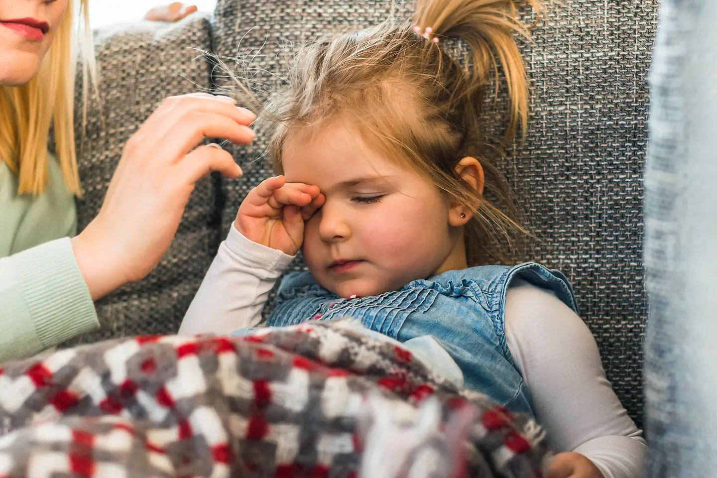 Ein kleines Mädchen liegt unter einer Decke und reibt sich das Auge