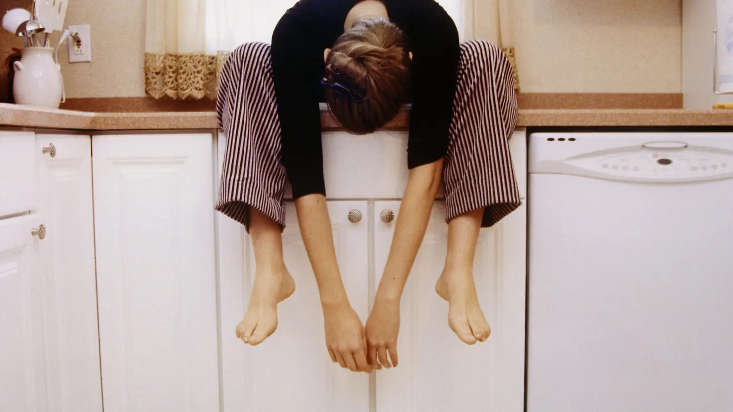 Junge Frau sitzt auf einem Küchenschrank und lässt den Kopf hängen