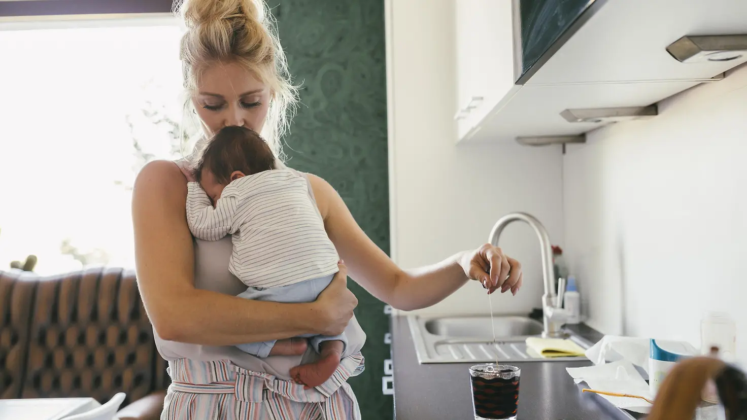 Mutter hält ihr Baby auf dem Arm während Sie in der Küche steht