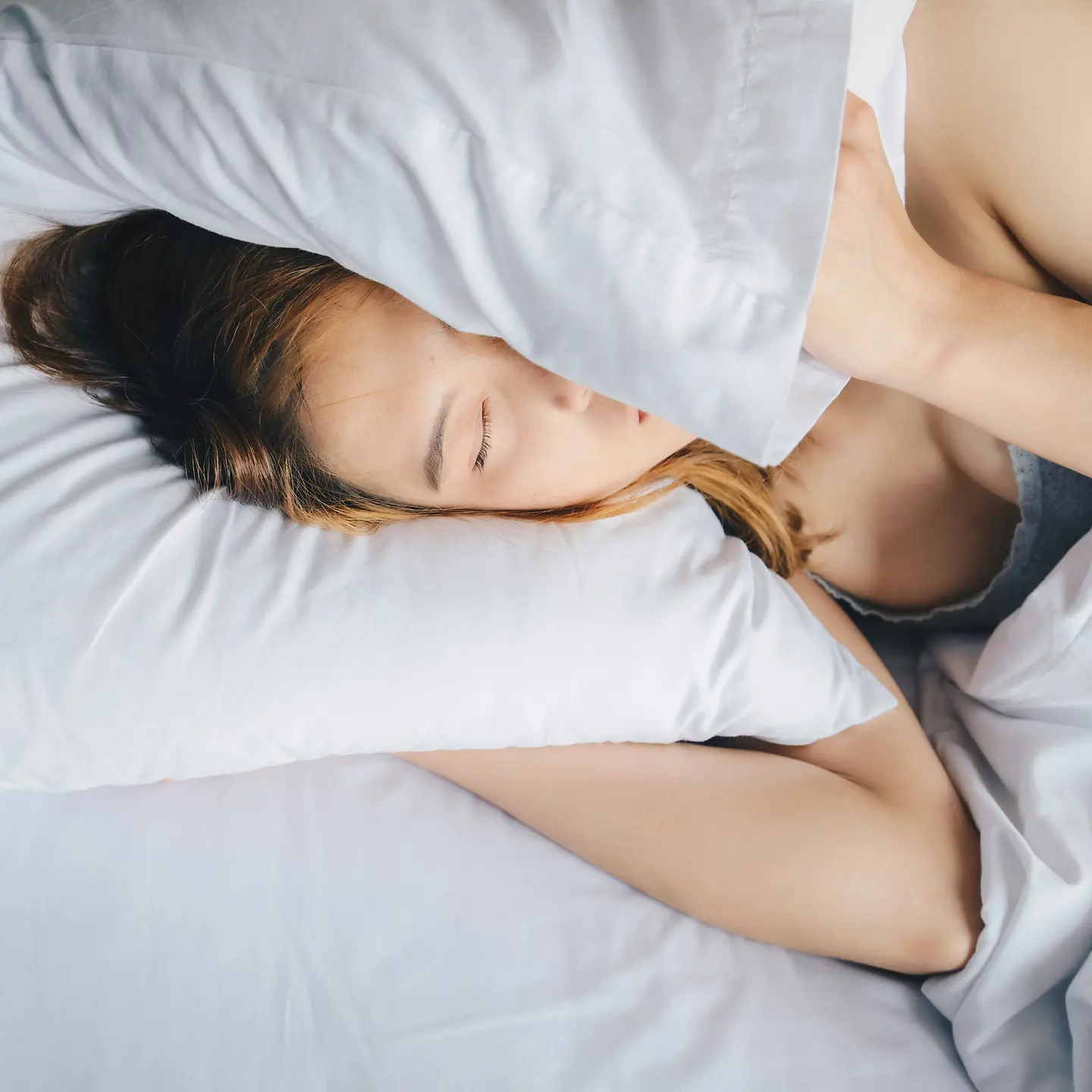 Eine Frau mit Schlafstörungen liegt im Bett und klappt ihr Kissen über den Kopf.