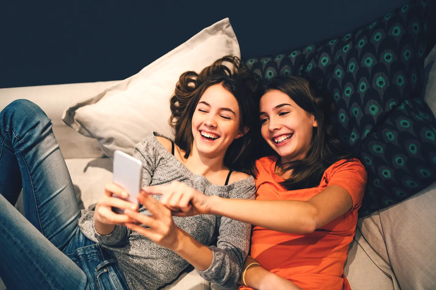 Zwei Jugendliche liegen auf dem Sofa und schauen auf ein Smartphone