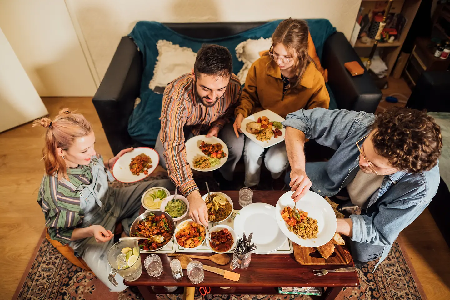 Freunde sitzen um einen Tisch und essen ein selbst gekochtes veganes Essen.