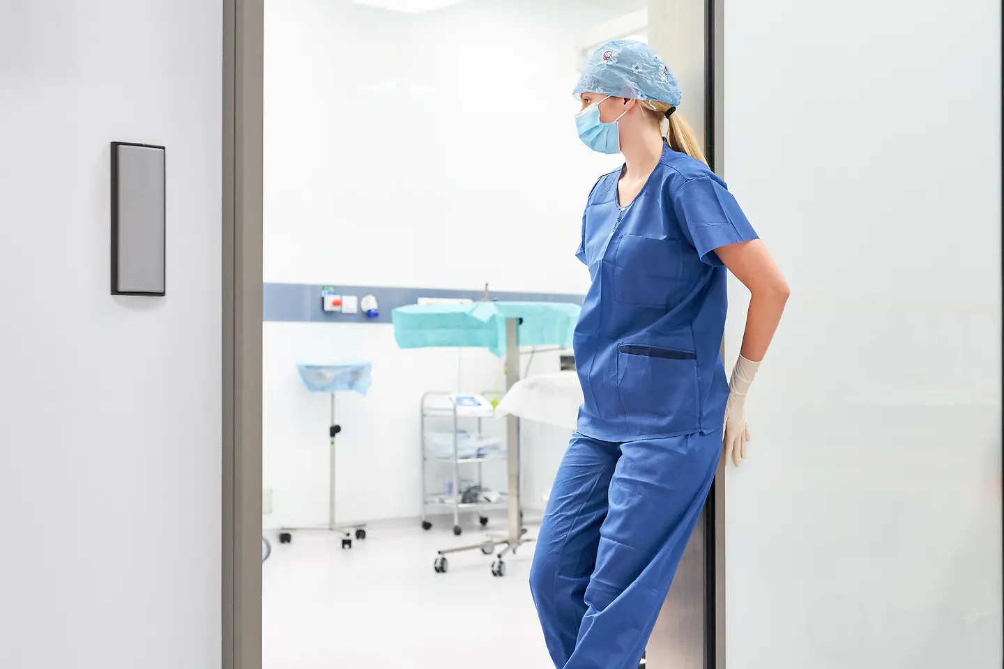 Zu sehen ist eine erschöpfte weibliche Pflegekraft im Eingangsbereich des OPs.