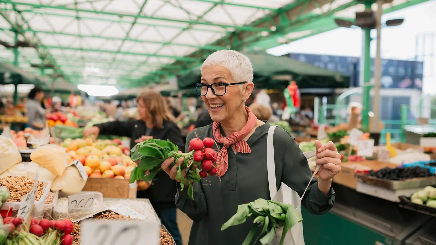 Lächelnde ältere Frau mit kurzen grauen Haaren kauft Lebensmittel auf dem Wochenmarkt ein