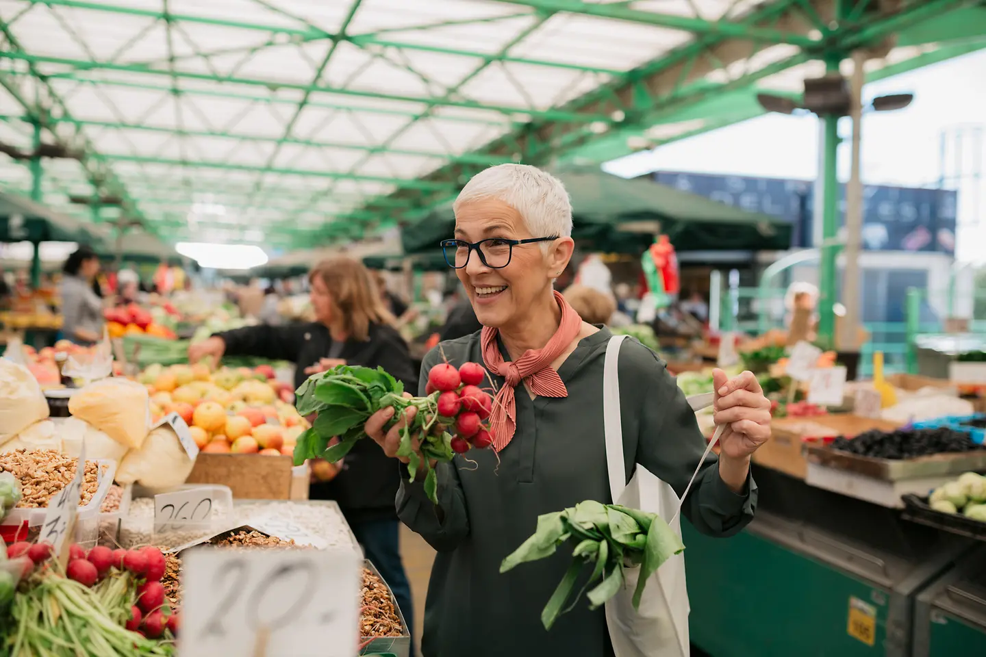 Lächelnde ältere Frau mit kurzen grauen Haaren kauft Lebensmittel auf dem Wochenmarkt ein
